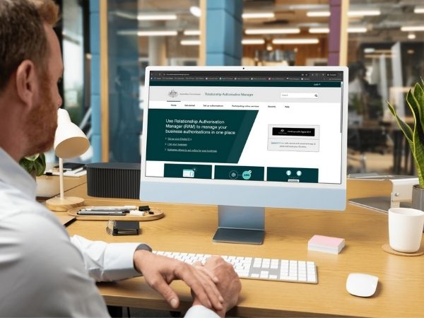Business owner at a desk accessing the Relationship Authorisation Manager (RAM) on a desktop computer to manage government access.